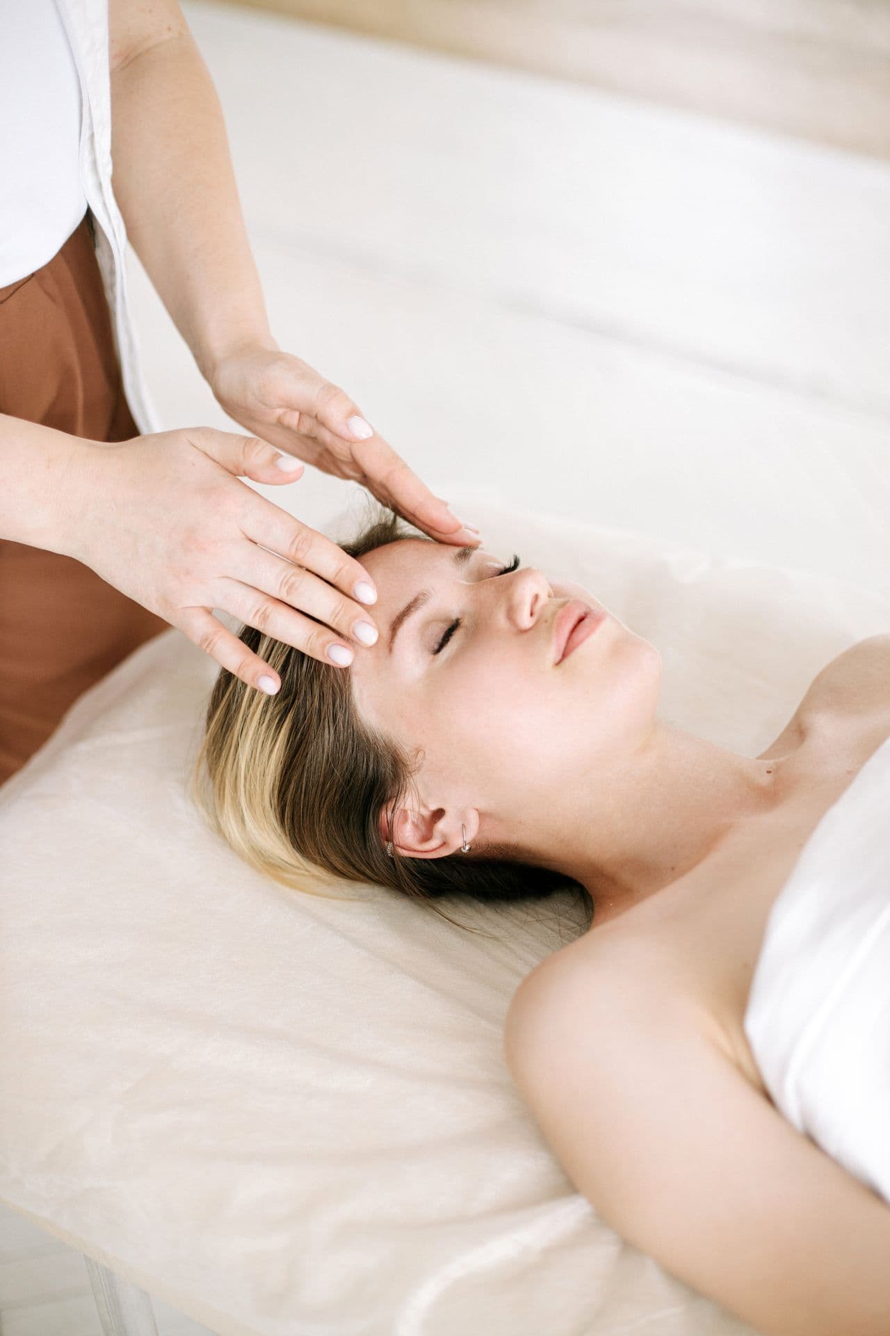 An experienced practitioner performing a relaxing facial massage in a soft, cream-toned treatment room
